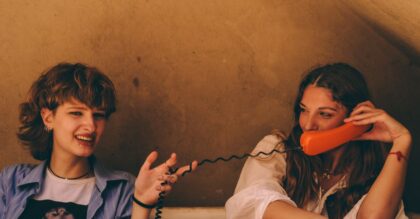 Two young women enjoying a fun chat using vintage orange phones indoors.